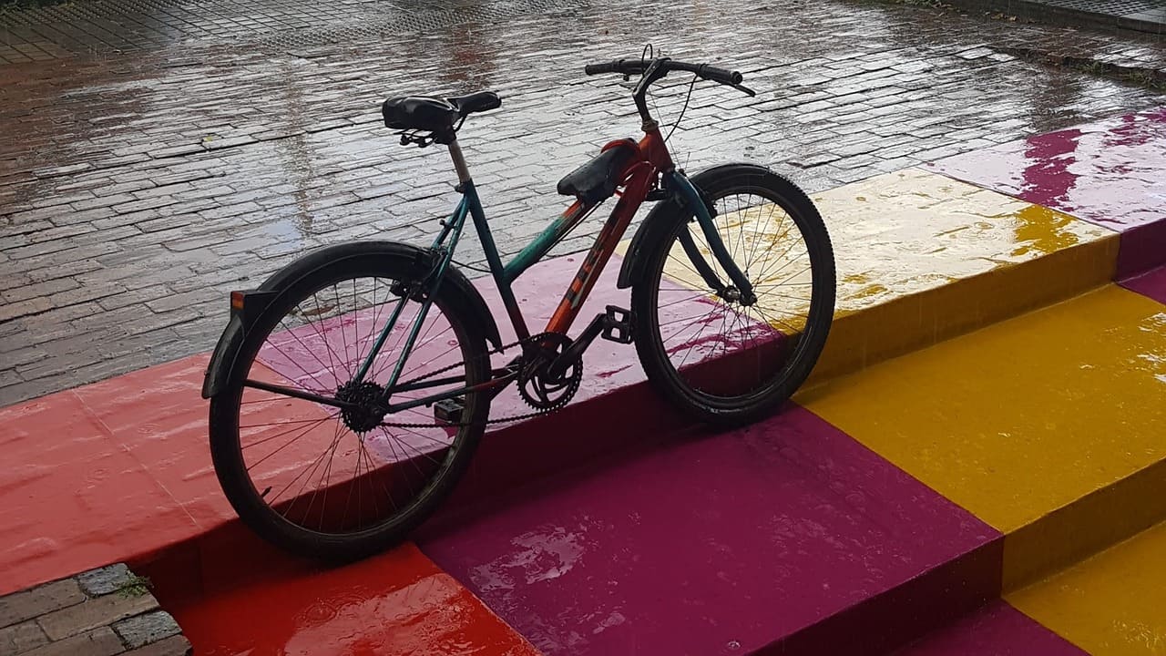 Bicycle rests against brick stairs. The stairs are playfully painted two shades of magenta and yellow. The brick is wet wit